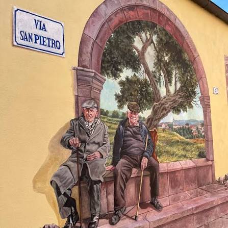 Murale di Pina Monne con due anziani seduti sotto un arco